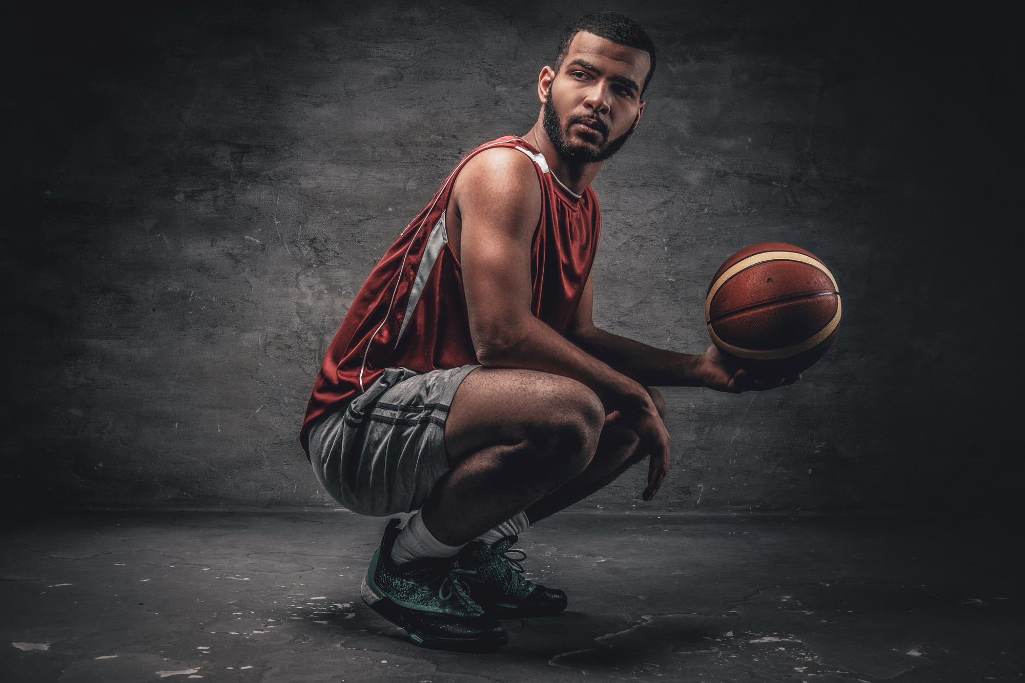 A black basketball player sits on a floor and holds basket ball.
