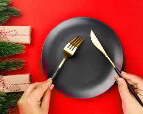 gold cutlery with black handles crossed over black plate on red table the concept of New Year dinner