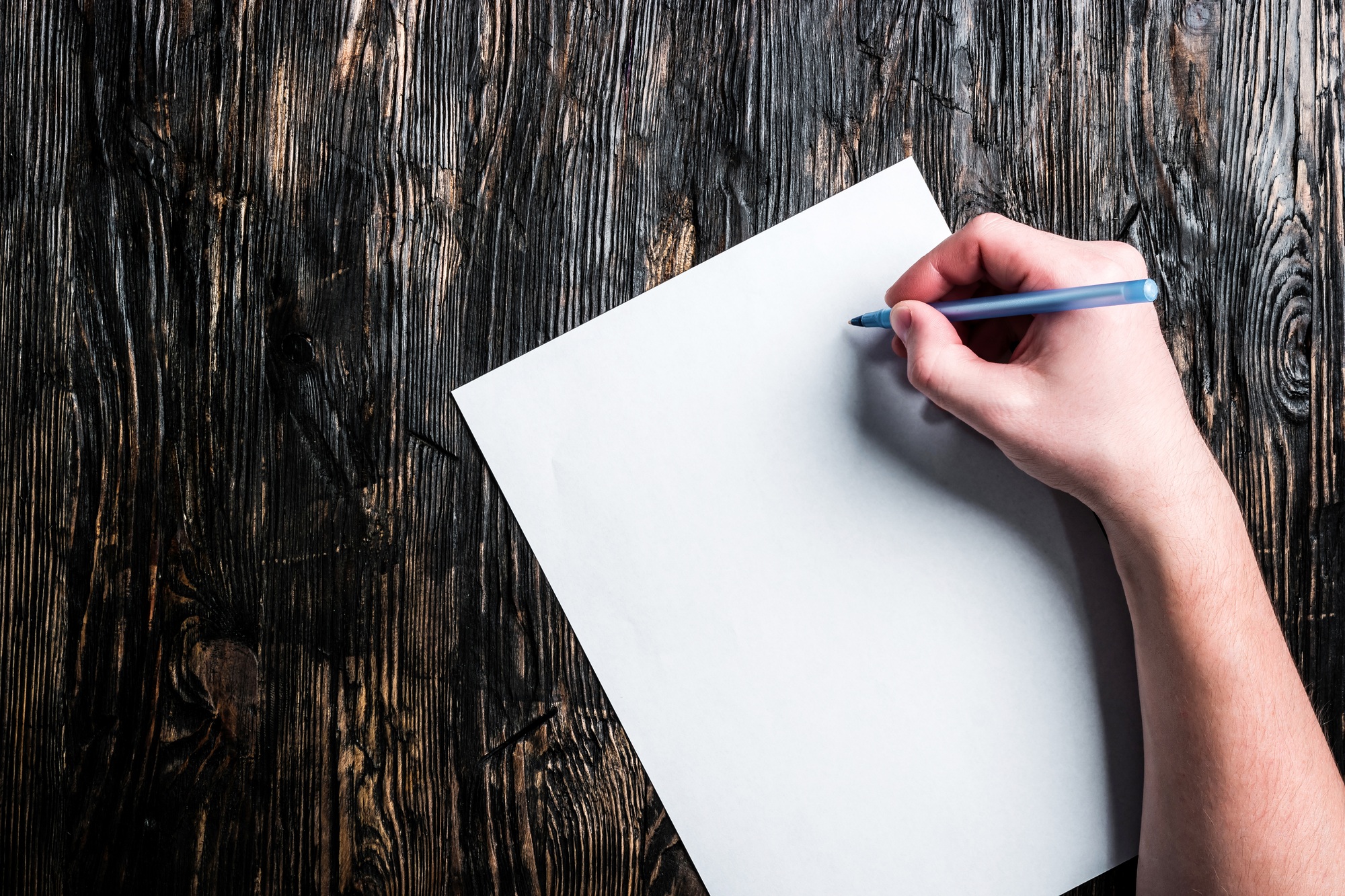 hand with pen and white blank sheet on table
