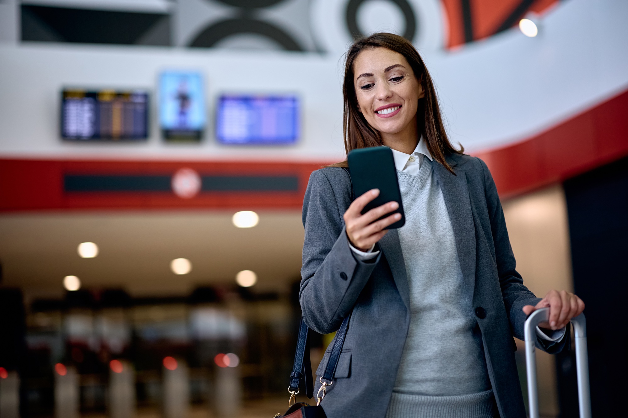 Happy businesswoman text messaging on cell phone at train station.