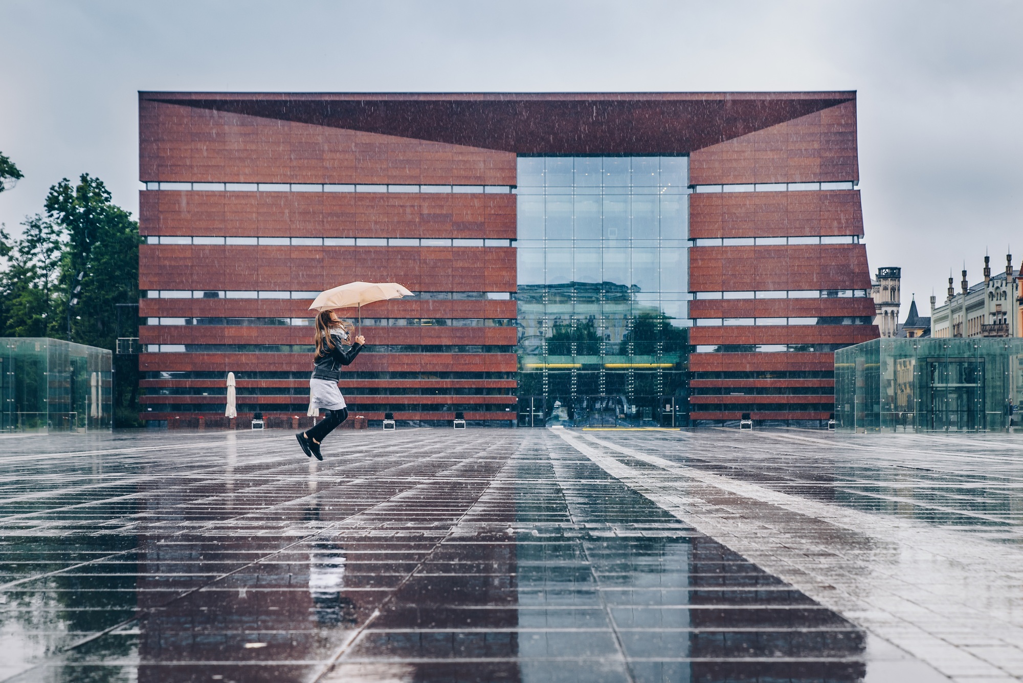 Scenic view of a little girl jumping with an umbrella in rain in Freedom Square, Poland