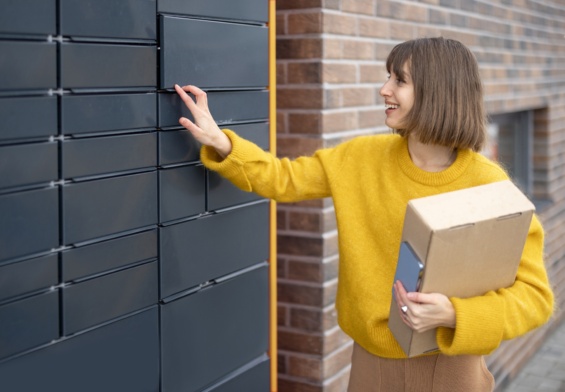 Woman getting parcel from cell of automatic post terminal outdoors